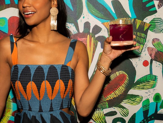 Woman holding cocktail in front of mural at Rumorosa San Diego